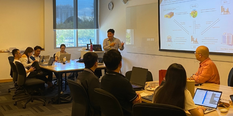 Photo of a guest lecturer presenting in front of the interactive whiteboard titling rice farmer ecosystem platform reco to the students who are sitting with their electronic devices