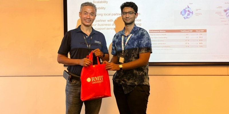 Photo of a guest lecturer being gifted an RMIT branded gift bag by a postgraduate student in front of the class