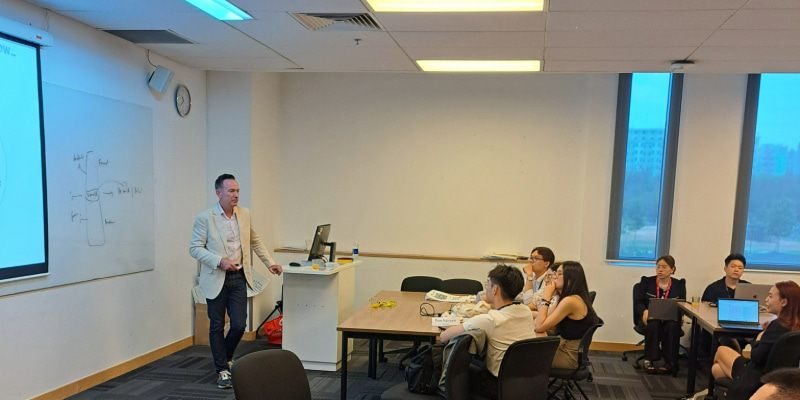 Photo of a lecturer teaching in front of a white board to a group of postgraduate students