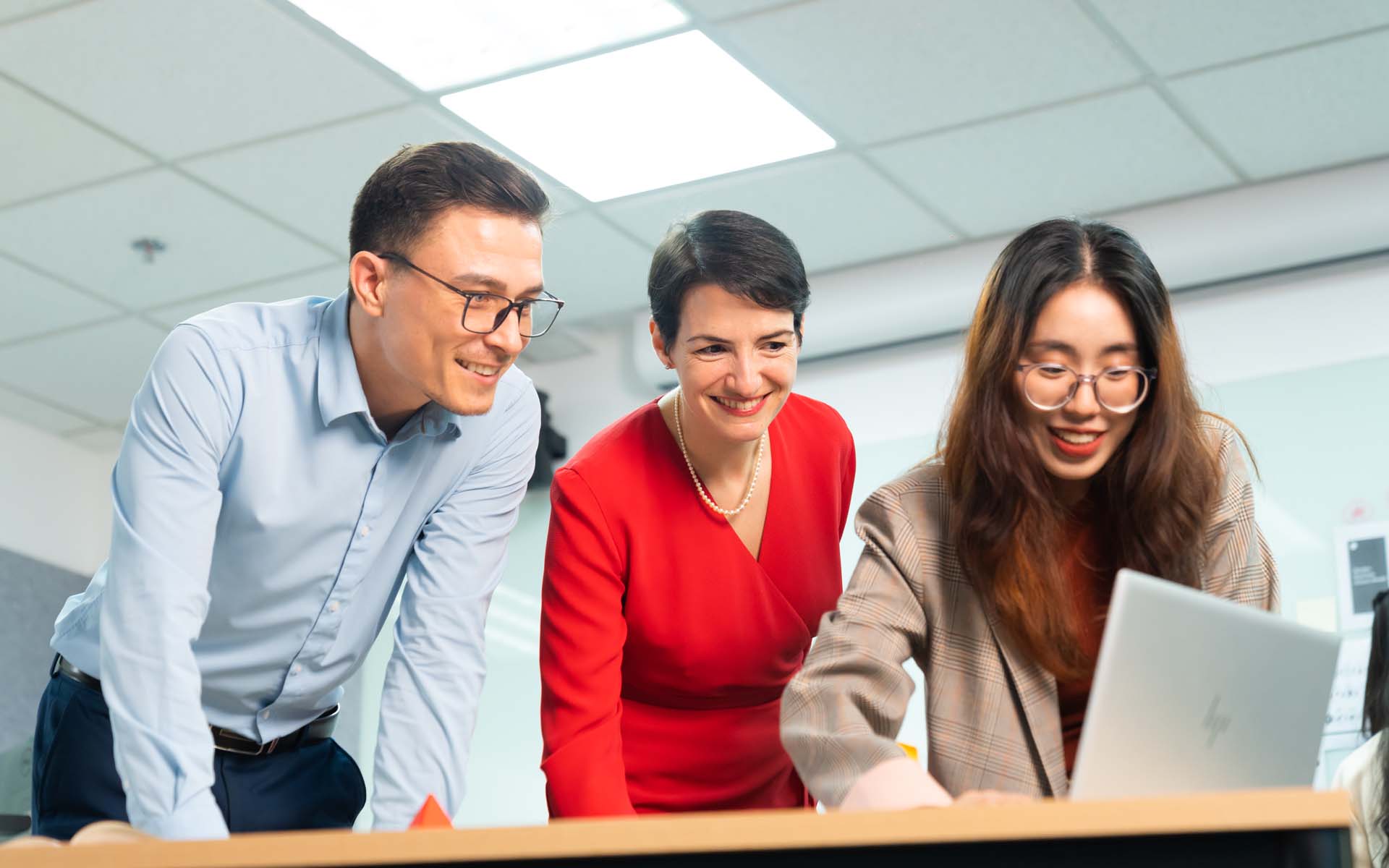 a male student and two lecturers one male and one female working in a meeting room with a laptop